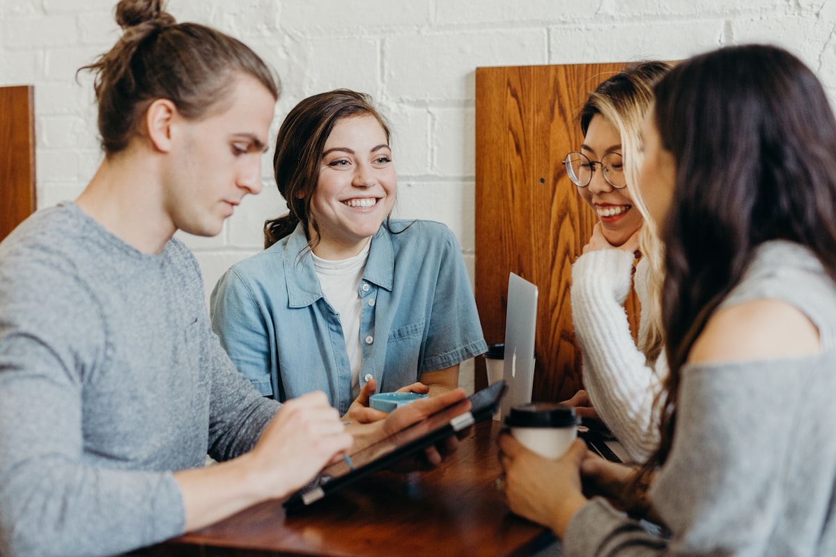 A multicultural team collaborates warmly around a laptop in a bright cafe setting.