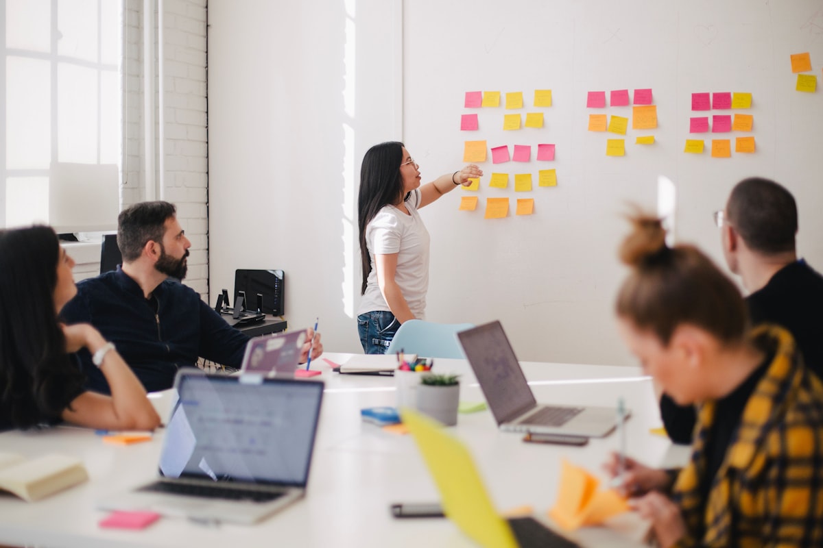 A team member reviews notes at a bright workspace, sticky notes spread across a wall.